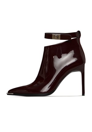 Burgundy patent leather ankle boot with pointed toe, high heel, and adjustable ankle strap featuring a metallic clasp. Smooth, glossy finish.