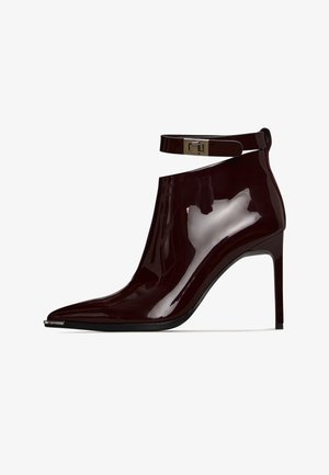 Burgundy patent leather ankle boot with pointed toe, high heel, and adjustable ankle strap featuring a metallic clasp. Smooth, glossy finish.