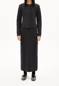 Cárdigan de punto gris oscuro con cinco botones, combinado con una falda larga a juego y zapatos decorativos con tachuelas. La tela tiene una textura suave.