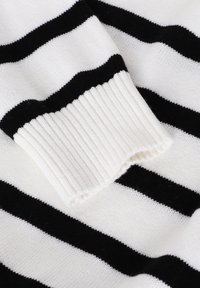 Gros plan sur un pull à rayures noir et blanc, avec un poignet en côte blanc, une texture douce et des rayures horizontales larges alternées.
