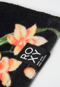 Tessuto nero con un motivo floreale che presenta fiori pesco e crema. Include un etichetta bianca "ROXY" prominente. Superficie strutturata.