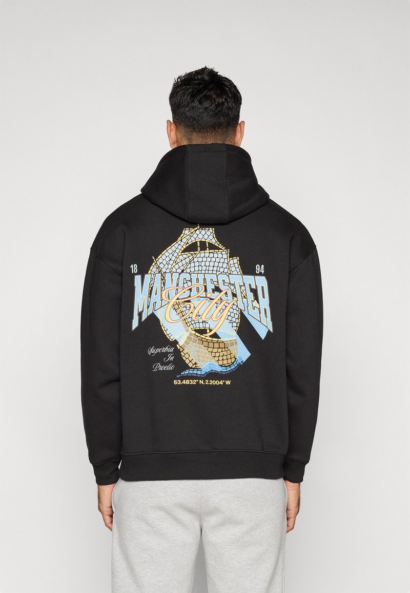 Musternööriga must kapuutsiga sviiter, millel on graafiline disain koos "Manchester City" tekstiga, koordinaatidega ja sinise ja kollase värvi aktsentidega.