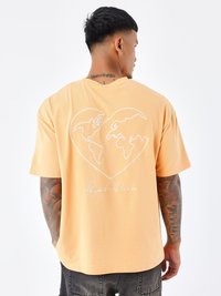 Oranje katoenen T-shirt met een witte hartvormige afbeelding van de wereld op de achterkant en de tekst "Project x Daries" eronder. Korte mouwen.