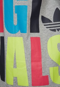 Gråbomullstyg med stora, färgglada bokstäver i rosa, blått, gult och svart. Har en Adidas-logotyp med tre ränder på ena sidan.