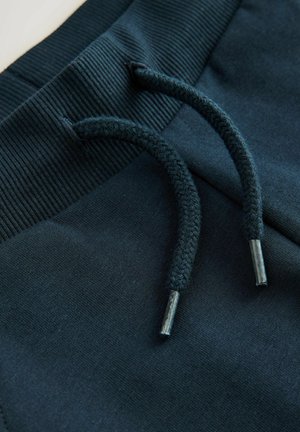 Pantalons de survêtement bleu marine avec une taille côtelée et un cordon tressé avec des embouts en métal, fabriqués à partir d'un matériau doux et texturé.