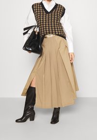 Rusettiharmaa houndstooth-neuleliivi, valkoinen paita sen alla, vaaleanbeige pliseerattu hame, mustat polvipituiset saappaat ja kiiltävä musta käsilaukku.