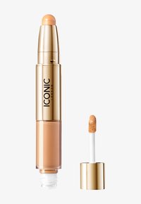 Concealerstift i gull- og beige emballasje med en avrundet spiss; inkluderer en separat applikator med en fluffy svampespiss.
