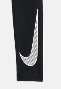 Svarte treningsleggings med et stort hvitt Nike-logo og diagonale striper. Laget av elastisk, glatt stoff med en figurnær silhuett.