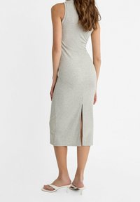 Robe midi grise ajustée, sans manches, avec une fente latérale. Confectionnée dans un tissu doux, elle présente une texture lisse et une coupe simple et épurée.