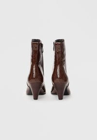 Botines de imitación cuero marrón con un patrón de cocodrilo, de altura corta y tacones de madera afilados. Cuentan con un cierre de cremallera lateral.