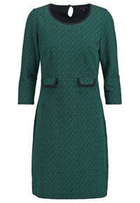 Vihreä tekstiilitakki, jossa on kolme neljännesosaa hihat, mustat yksityiskohdat ja avara pääntie, jossa on avainreikäleikkaus. Sisältää etutaskut.