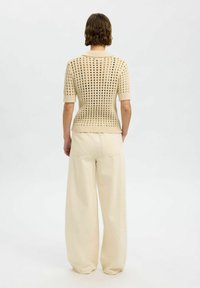 Pull en tricot crème à manches courtes avec un motif ouvert texturé, associé à un pantalon beige à jambes larges. Vue arrière affichée.