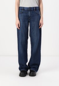 Dark blue denim wide-leg jeans with a mid-rise waist, featuring front pockets and contrasting stitching. Worn with black footwear.