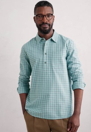 Light blue and white gingham shirt, long sleeves, collar, button-up front, with a chest pocket. Worn with khaki trousers.