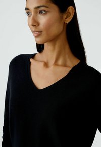 Schwarzer gestrickter Pullover mit V-Ausschnitt, langärmlig und mit einer weichen Textur, präsentiert an einem Modell vor einem neutralen Hintergrund.
