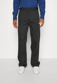 Schwarze Hosen mit geradem Bein, aus glattem Stoff, mit flachem Bund und elastischem Taillenbund. Kombiniert mit weißen Sneakers.