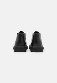 Botas de tobillo de cuero negro con un acabado suave, punteras redondeadas y una suela gruesa de goma. Presentan un sutil detalle en la cremallera trasera.