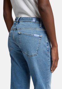 Jeans in denim azzurro chiaro con taglio dritto, cuciture visibili, due tasche posteriori e un piccolo logo sul cinturino.