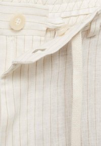 Gros plan sur un tissu beige à fines rayures avec deux boutons beiges et un détail de boucle en tissu.