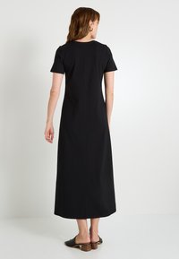 Robe maxi noire à manches courtes avec une coupe droite, dotée d'une couture subtile dans le dos et associée à des mules noires à petit talon.