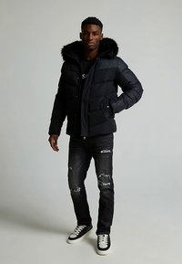 Puhasta vetrovka v temno modri barvi z obrobo z lisjim krznom, s šivanim vzorcem in dvema stranskima žepoma, kombinirana z raztrganimi črnimi jeansami in supergami.