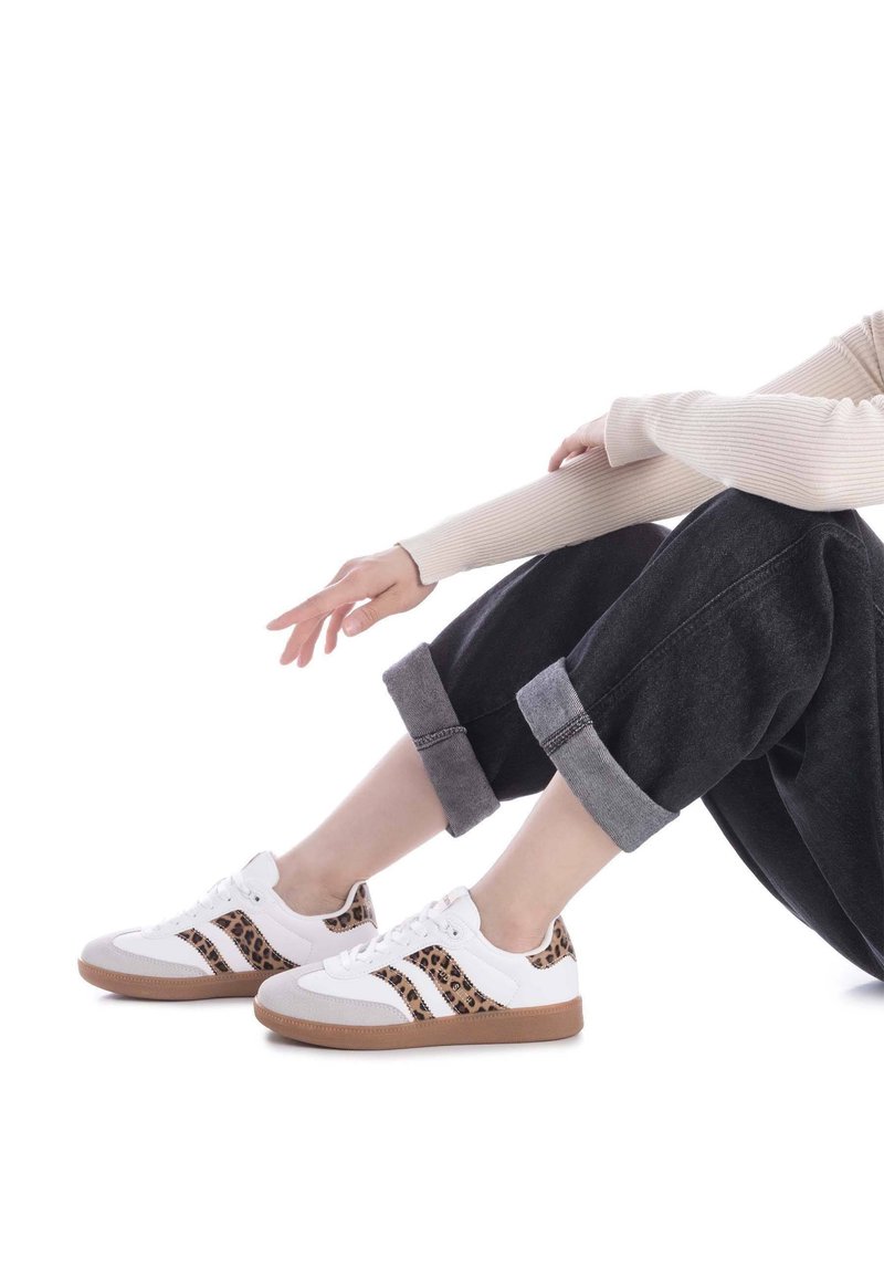 Zapatillas blancas con acentos de estampado de leopardo, puntera gris y suela de goma marrón. Combinadas con pantalones negros cortos con dobladillos enrollados.