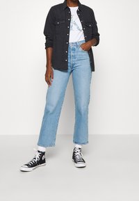 Camisa de mezclilla negra de botones sobre una camiseta gráfica blanca, jeans de tiro alto de color azul claro y zapatillas de lona altas negras con acentos blancos.