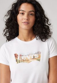 Witte katoenen t-shirt met een kleurrijke landschapsafbeelding en de tekst "Levi's" in opvallende witte letters, ronde halslijn en korte mouwen.