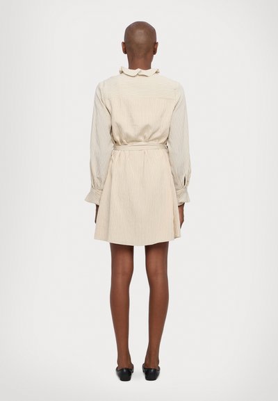 Beige striped dress with a fitted waist, long sleeves, and a ruffled collar. Features a short skirt and black footwear. Back view.