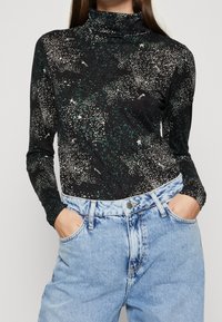 Zwarte coltrui met een sterrenprint in wit en groen, lange mouwen en zachte stof, gecombineerd met hooggerande verouderde blauwe jeans.