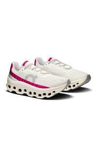 Un paio di scarpe sportive bianche e rosa con suole spesse e ventilate e lacci decorati, posizionate a un lieve angolo su uno sfondo bianco.