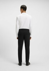Biała koszula z długim rękawem w połączeniu z czarnymi spodniami formalnymi. Spodnie mają gładką teksturę i dopasowany krój z tylnymi kieszeniami.