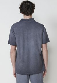 Chandail à manches courtes, gris foncé, fabriqué en tissu léger et texturé. Il présente un col et un ourlet arrondi, avec une coupe décontractée et un motif subtil.