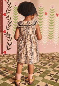 Leoparda raksta kleita ar melnu volānu apkakli un savāktu vidukli. Kombinēta ar rozā zeķēm un brūnām sandales. Ziedu fons.
