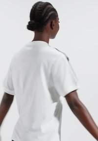Vit kortärmad t-shirt med avslappnad passform, med en mjuk textur och en subtil design på baksidan och axeldekorationer.