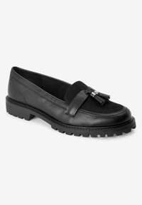 Schwarze Lederhalbschuhe mit einem Wildlederband und Quasten-Detail. Sie haben eine dicke, strukturierte Gummisohle für guten Halt. Glatte Oberfläche, abgerundete Form.