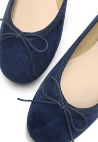 Ballet flats en daim bleu marine avec un bout rond et un nœud décoratif, présentant une tige texturée et une doublure intérieure lisse.