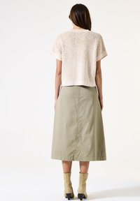 Gehaakte top met korte mouwen in roomkleur, met een gestructureerd patroon; gecombineerd met een knielange, olijfgroene rok, gedragen met beige enkellaarsjes.