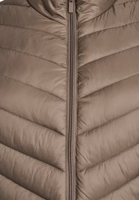 Hnedá vypchávkovaná vesta s vysokým golierom, horizontálnym prešívaným vzorom a centrálnym zipsom. Hladká, lesklá textúra s moderným dizajnom.