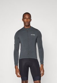 Jersey de cyclisme gris à manches longues avec une fermeture éclair à l'avant et le logo "LE COL", associé à un cuissard de cyclisme noir. Texture lisse, design ajusté.