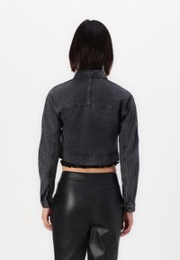 Przycięta czarna kurtka dżinsowa z postrzępionym dołem, zapinanymi mankietami i klasycznym kołnierzem; przedstawiona z tyłu. Połączona z dopasowanymi spodniami skórzanymi.