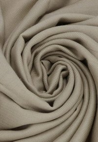 Tessuto beige disposto a spirale, caratterizzato da una texture liscia e un delicato motivo a spina di pesce, che trasmette un aspetto morbido e caldo.