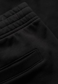 Pantaloni da allenamento neri con una vita testurizzata caratterizzata da cuciture orizzontali e una tasca posteriore discreta per riporre gli oggetti. Materiale morbido con elasticità.