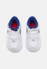 White leather sneakers with blue accents, red interior, and perforated detailing. Features laces and a branded logo on the tongue.
