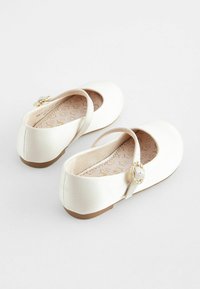 Ballerines blanches en tissu lisse avec un bout arrondi, une sangle de cheville et un détail décoratif de boucle en or sur la sangle.