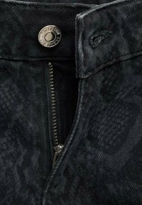 Svart denimtyg med ett texturerat mönster, med en silverknapp och dragkedjestängning. Midjebandet har bältesöglor.