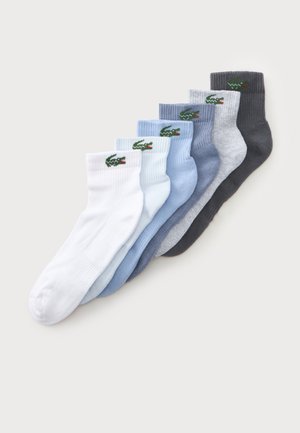 Sept paires de socquettes en blanc, bleu clair, bleu, gris et gris foncé, chacune avec un logo crocodile vert près du bord-côte.