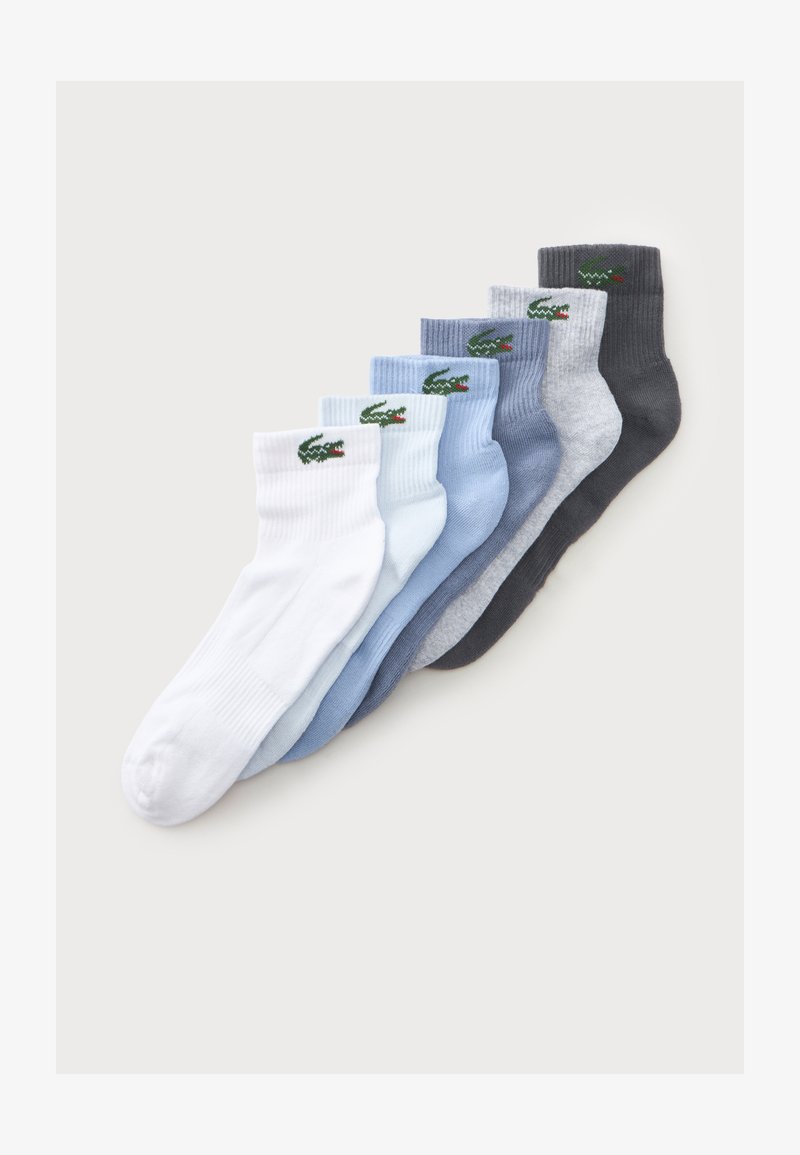 Sept paires de socquettes en blanc, bleu clair, bleu, gris et gris foncé, chacune avec un logo crocodile vert près du bord-côte.