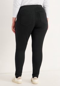 Zwarte legging met een hoge taille, achterzakken en een nauwsluitend ontwerp. Gecoördineerd met witte sneakers met een logo aan de zijkant.