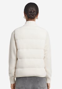 Weste aus Steppmaterial mit geribbeltem Kragen und Bündchen, ausgestattet mit einer strukturierten weißen Strickfront und glatten, gepolsterten Rückenteilen.